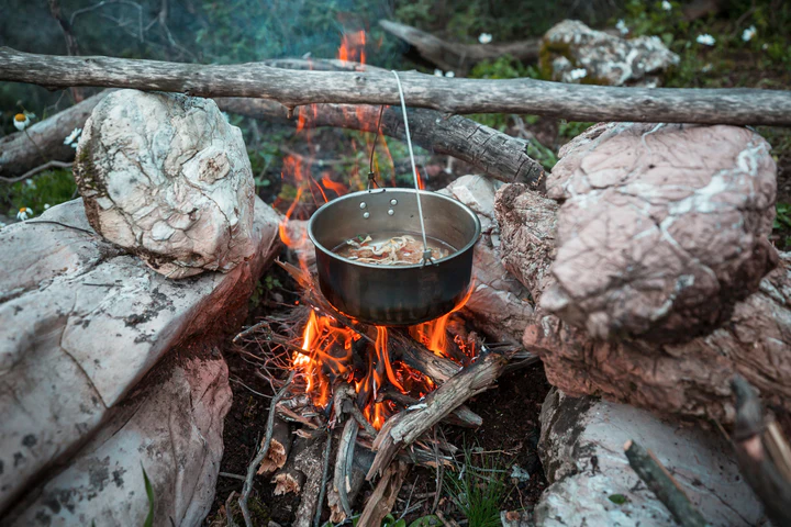 Cookset on fire in a wild setting, demonstrating outdoor cooking for a Wild Survival Guide.