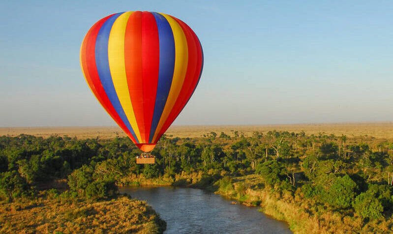 Hot air balloon flying over a river in Maasai Mara National Reserve, Kenya